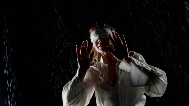 strange blindfolded woman enjoying rain in night, touching water drops by hands, madness and inspire