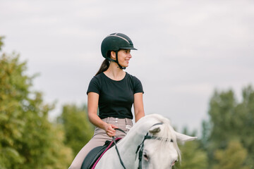 Pretty girl, a horseback rider riding beautiful snow white horse, walking along a path on a sunny summer day