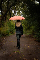 A girl walking in the park under an umbrella in the fall. A red umbrella in the fall