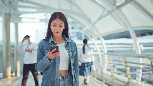 Happy young asian woman using mobile phone with chatting online with friends, Female in jean jacket walking in the city using social media on smartphone, Technology