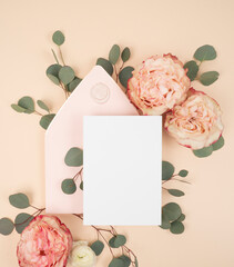 Bridal stationery flat lay with a blank invitation card and blush envelope and fresh roses and eucalyptus