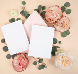 Flat lay with two blank stationery invitation cards and pink envelope and fresh roses and eucalyptus