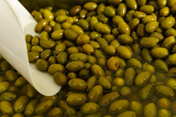 Seasoned olives with marinade and a white spatula in a container on the counter.