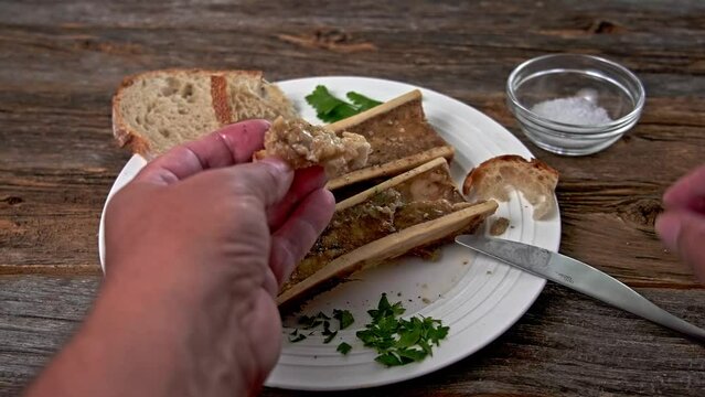 Eating roasted marrow bones  fat with bread from plate on rustic table
