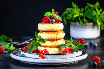 Thick pancakes with cottage cheese, blueberries, raspberries and red currants, decorated with fresh mint delicious breakfast. Black table background