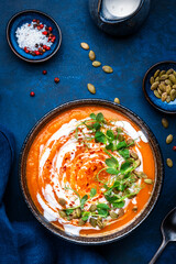 Autumn pumpkin puree soup with seeds, cream and green pea sprouts. Winter healthy vegetarian slow comfort food. Soup bowl on blue table background. Top view