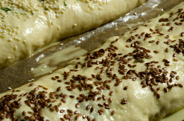 Pie with meat. A roll of yeast dough, sprinkled with flax and sesame seeds, on parchment.