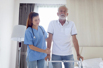 Female nurse or doctor helping elderly patient man lean to walk with orthopedic walker, patient practice walking inside house with physiotherapist, nursing senior people at house, medical health care.