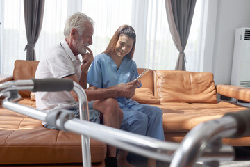Fototapeta premium Female nurse takes care of senior patient and teaches him to use digital tablet at living room house, elderly mature grandfather learns to online internet and high-tech, nursing medical health care.