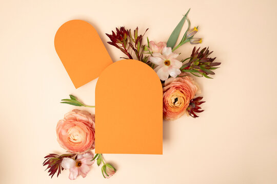 Wedding stationery flat lay with arched orange blank invitations and fresh ranunculus flowers