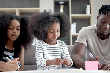 Happy family love bonding, African father and two daughter girls with curly hair enjoy spending time together at home, little child kid and father make hand drawing paper craft card and eating snack.