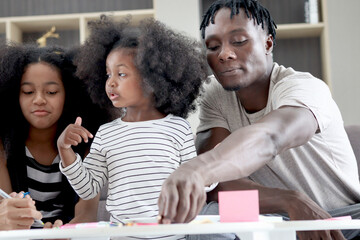 Happy family love bonding, African father and two daughter girls with curly hair enjoy spending time together at home, little child kid and father make hand drawing paper craft card and eating snack.