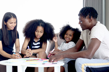 Happy family love bonding, African father mother and two daughter girls with curly hair enjoy spending time at home, little kids and parents make hand drawing paper craft card together in living room.