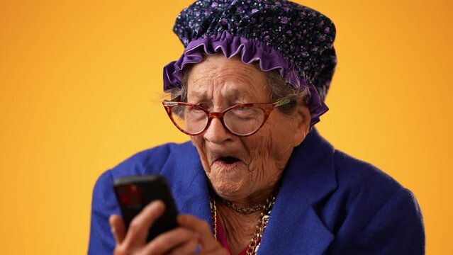 Closeup of toothless funny old crazy grandmother wearing glasses isolated on yellow background talking on phone.