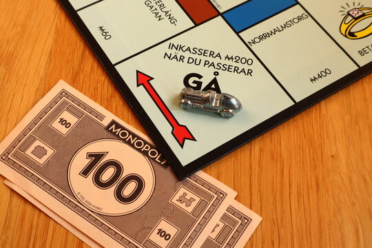 Monopoly board game. Passing go or the start. Metal car token parked. Close up and isolated, wooden background. Collect money. Written text in Swedish. 
