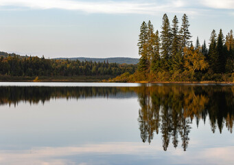 Fototapeta na wymiar Mirror-like reflections on a lake of the autumn scenery of a Canadian forest with vibrant colors
