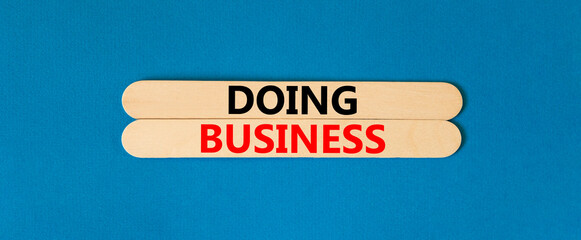 Doing business symbol. Concept words Doing business on wooden stick. Beautiful blue table blue background. Business, motivational Doing business concept. Copy space.