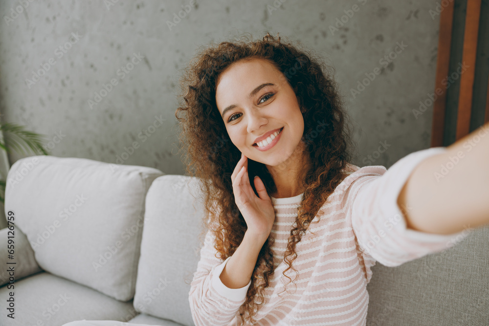 Wall mural close up young woman wear casual clothes sits on grey sofa couch do selfie shot pov on mobile cell p