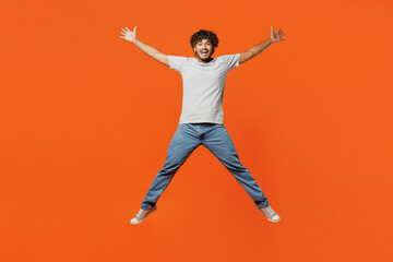 Fototapeta na wymiar Full body young overjoyed excited smiling happy Indian man he wears t-shirt casual clothes jump high with outstretched legs hands look camera isolated on orange red color background studio portrait.