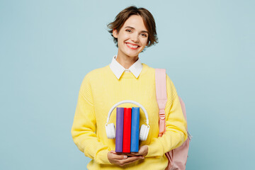 Young smiling fun woman student wear casual clothes yellow sweater backpack bag hold pile of book...