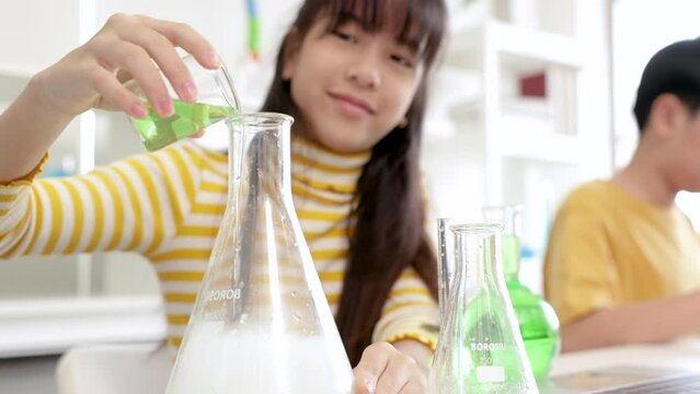 Asian elementary boys and girl school kids students have fun studying sitting in laboratory classroom enjoy mixing liquid substance experiments, education happy learning by doing in private school