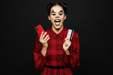 Young cool woman with Halloween makeup face art mask wear clown costume red dress hold use mobile cell phone credit card isolated on plain black background studio portrait Scary holiday party concept