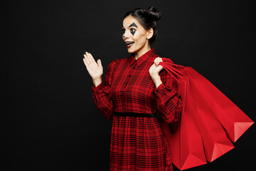 Young cool woman with Halloween makeup face art mask wear clown costume red dress hold shopping package bags isolated on plain black background studio Scary holiday party concept sale buy day concept