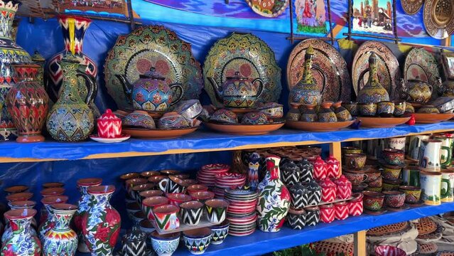 Uzbek national ceramic tableware in Tashkent - June 29, 2023: Goods at the Oriental Bazaar in Uzbekistan. Chorsu Market. Plates, teapots, cups. Painting with floral ornament. 4K