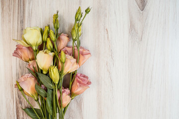 Bouquet of cream and apricot colored lisianthus flowers placed at the left of the image. Light wood background. Space for text at the right.