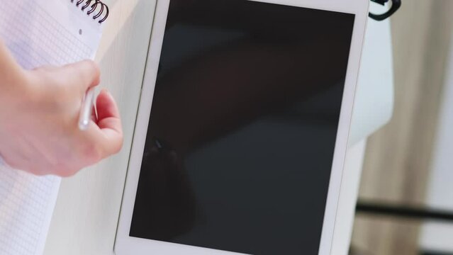 Vertical video. Online conference. Virtual meeting. Business woman working on project at tablet with empty space black mockup screen writing instructions with pen in hand at desk.