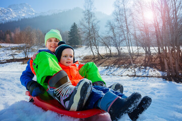 Two kids, brothers, slide downhill on the alpine slope together