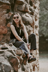Attractive east asian woman in black sunglasses and black clothes sitting on ancient stone wall