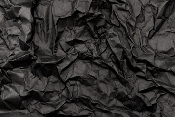 A sheet of black crumpled paper with folds and wrinkles. Dark paper texture