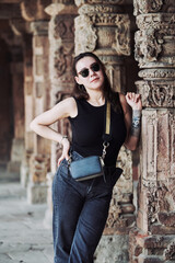 Attractive east asian woman in black sunglasses and black clothes stands among ancient pillars