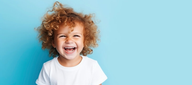 Plump handsome child todler boy with curly hair laughs with his eyes closed in joy in white T-shirt on blue background. Happy baby, childish joy. Concept of people's emotions