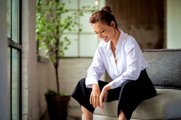 Shot of a mid aged woman wearing white shirt and black pants and relaxing in the armchair