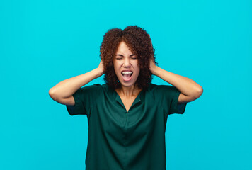 Frustrated and nervous African American business woman holds her head and screams hysterically in panic standing isolated on blue color background