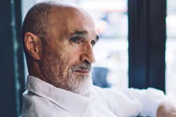 Thoughtful old businessman siting at table surfing tablet in cafe