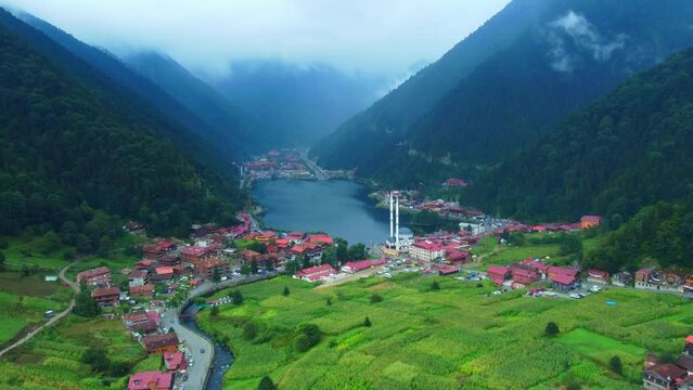 Aerial view to Uzungol lake natural lake in mountain in city of Trabzon Turkey. Aerial drone flying over large mountain forest hill, revealing beautiful lake and mosque in village on cloudy day.