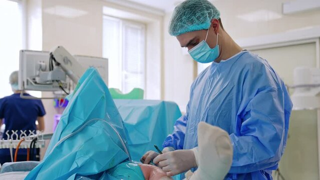 Confident male surgeon sewing the patient at the end of operation. Female nurse assisting.