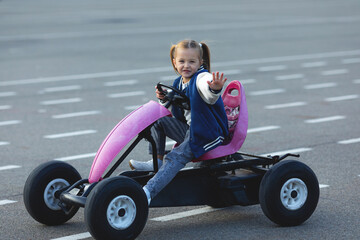 Little girl is riding on pedal karting. Child on a toy pedal car rides on a bike path outdoor, active children's vacation