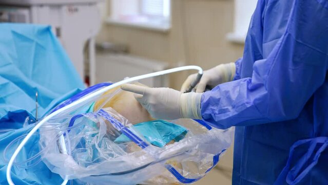 Knee operation with the help of laparoscopic instruments. Gloved hands of unrecognized doctor hold the tool.