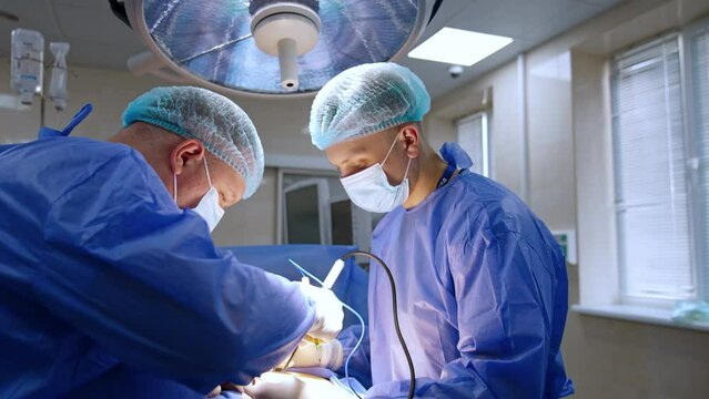 Careful male surgeon uses electric tool producing smoke. Place of operation is lit with bright light.