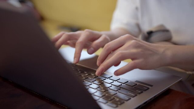 Close up view of hands of young girl typing text on silver laptop. woman writes letter or enters query on Internet into search engine. Online education. Correspondence in online messenger.