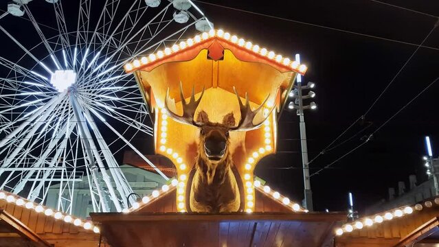 Christmas market. Celebrating New Year in Europe.  Festive stalls with Christmas lights, Ferris wheel. Interactive stuffed moose head at traditional Holiday fair. Magical atmosphere of winter holidays
