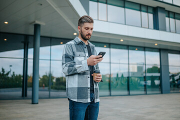 A confident young man with a smartphone, browsing the internet outdoors in an urban setting. Confident Young Man Exploring Cyberspace in Urban Oasis