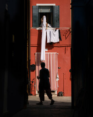 silhouette of a person walking down Burano streets with colorful houses and drying laundry