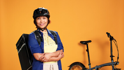 Portrait of courier folding her arms, proud of fast delivery to customer. Bike rider transporting food and other perishable items to clients using thermic backpack, isolated over studio background