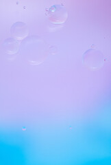 Abstract background in blue and lilac soft tones. Macro drops of oil on the surface of the water. Delicate cosmetic background for advertising products. Vertical photo