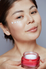 modern asian woman with facial cream jar and eye cream on face